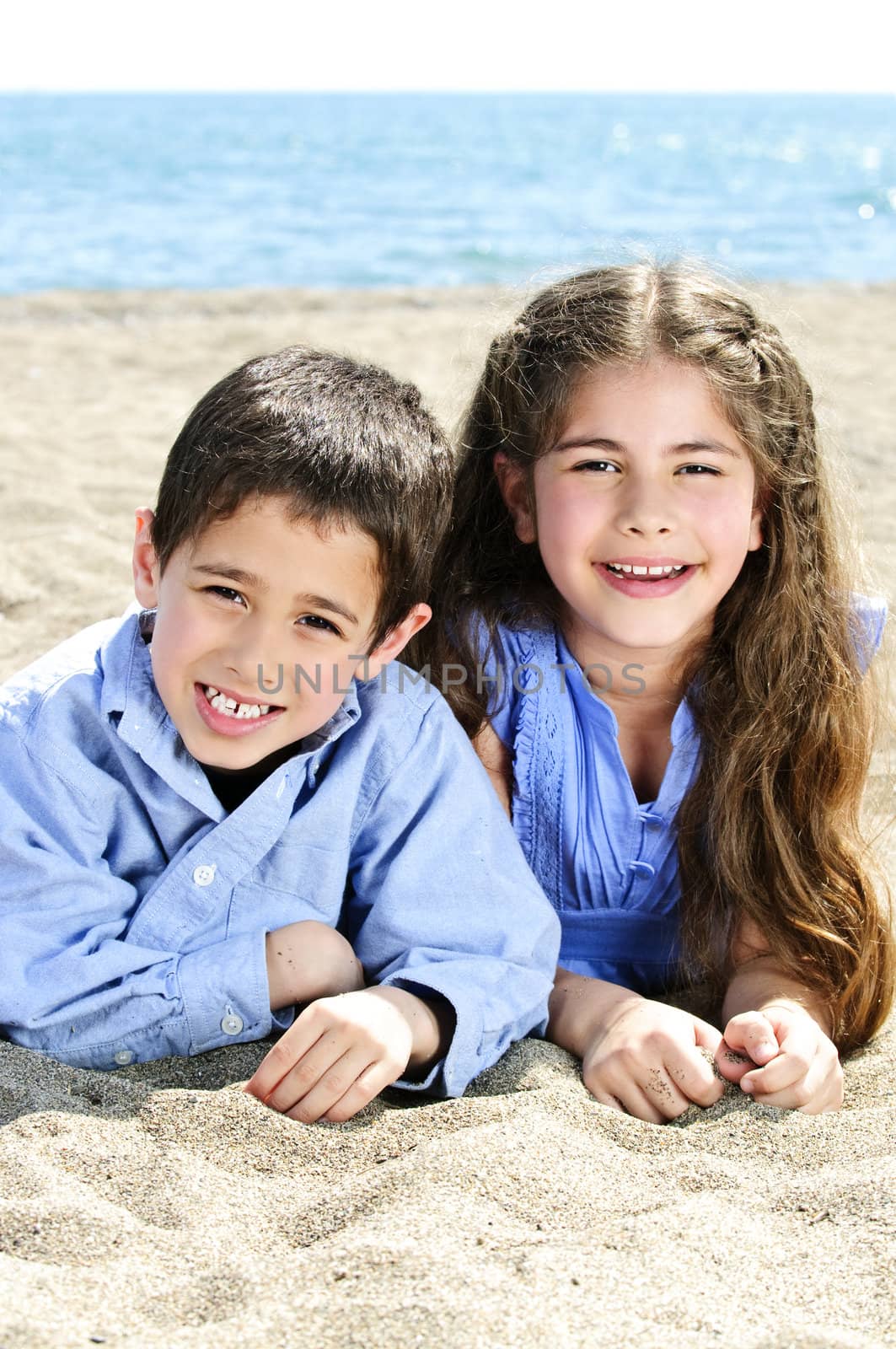 Portrait of brother and sister laying on sand at the beach