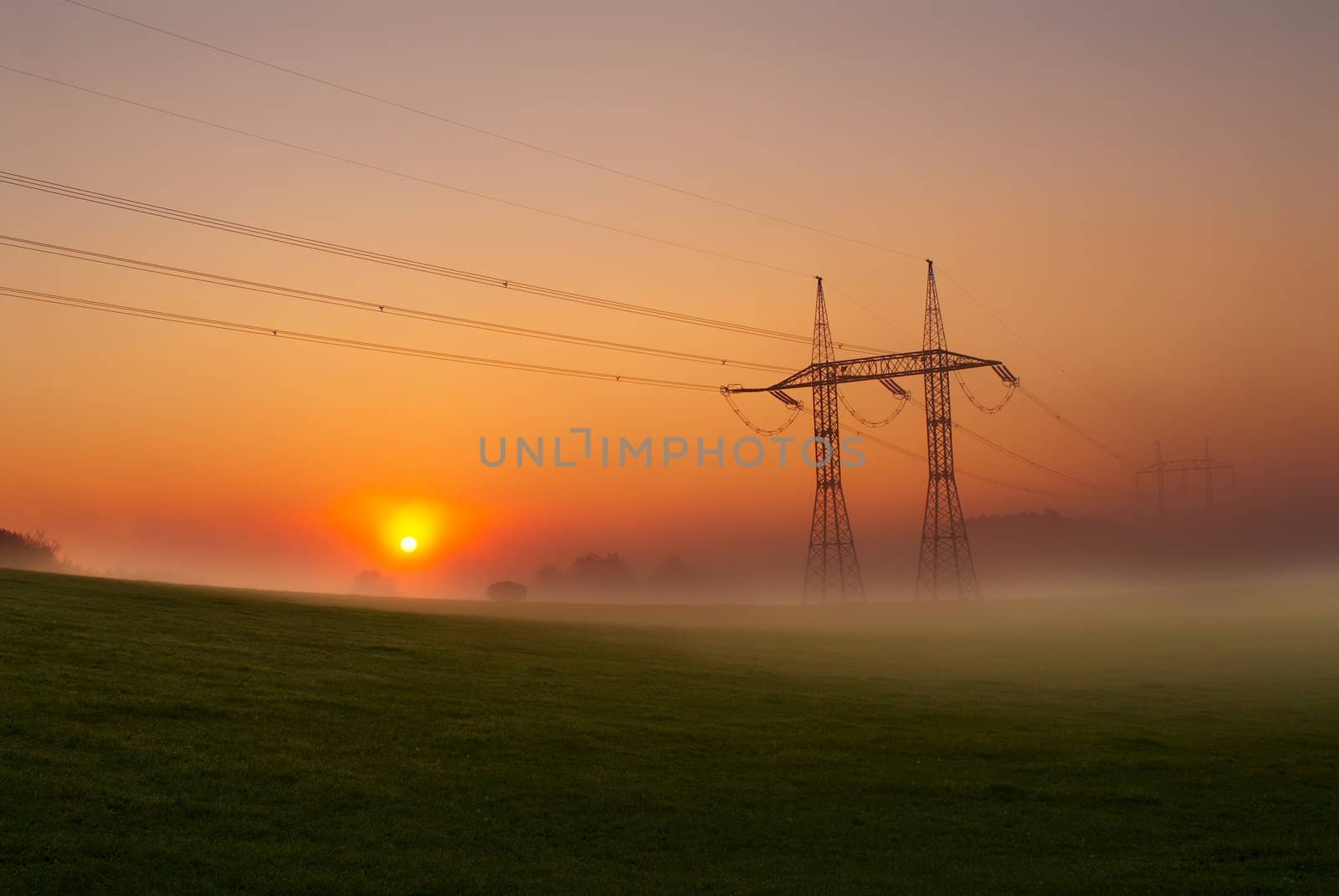 Foggy summer morning. Electricity pylons against a rising sun