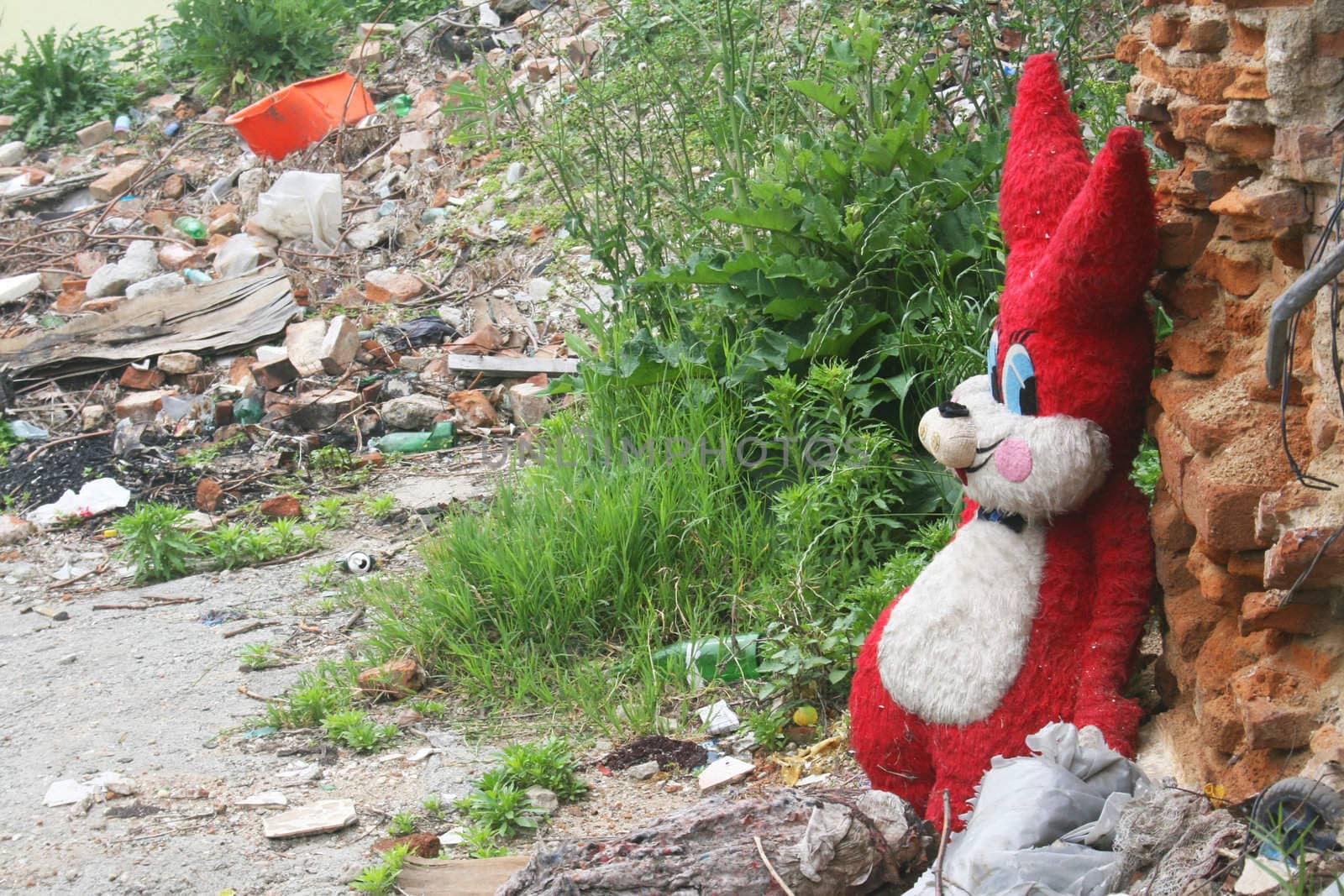 Giant red stuffed bunny in garbage filled deserted city lot