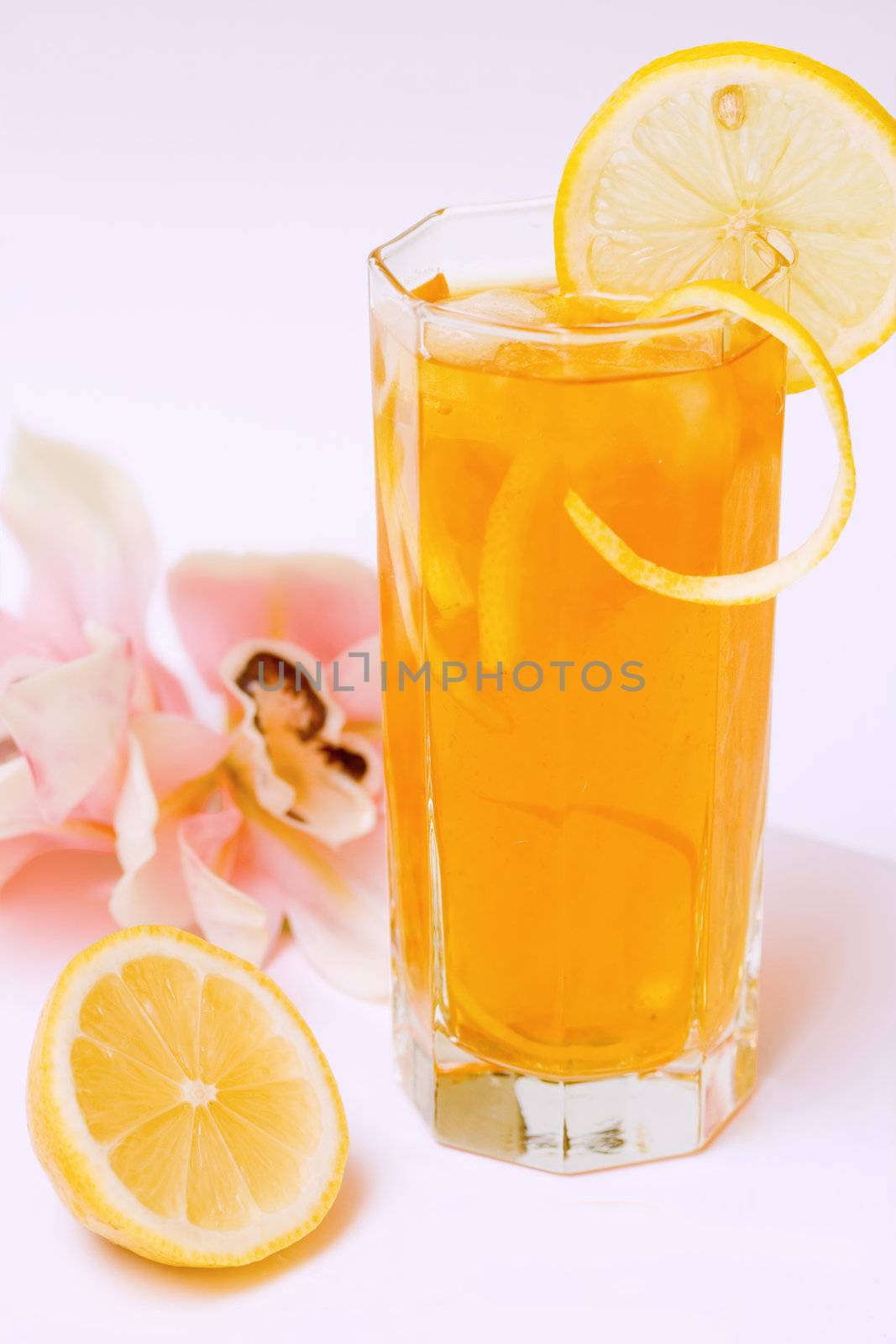 A glass full of iced tea with a lemon slice and orchid in background