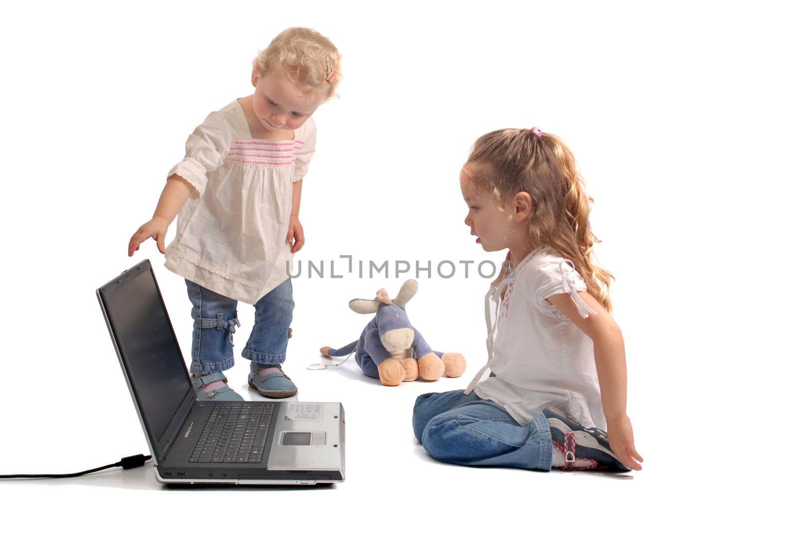 Little girl and her baby sister, bored of playing with toys, waiting for the notebook turns on