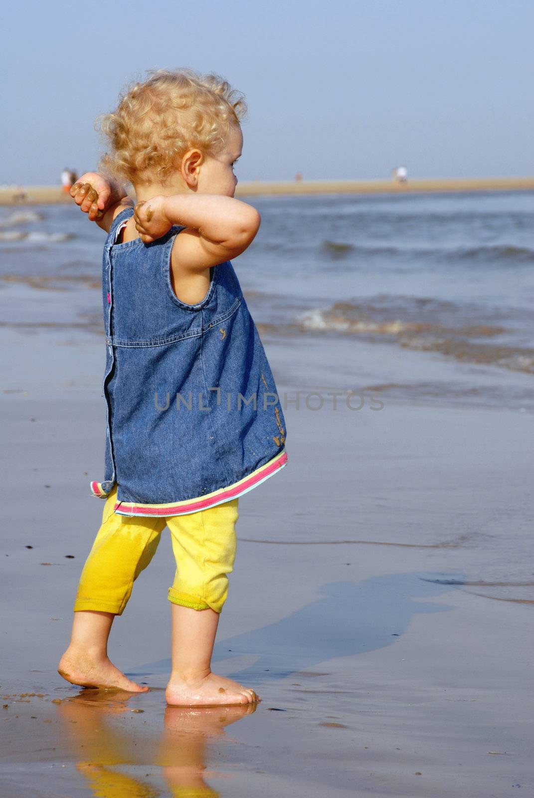 Little girl dressed at the seashore about to throw wet sand into the sea