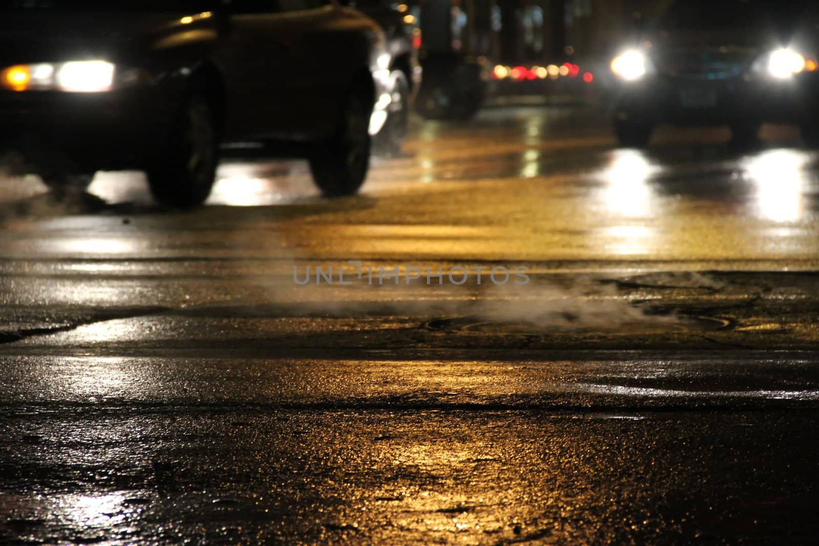 Cars moving on a wet city street at night.