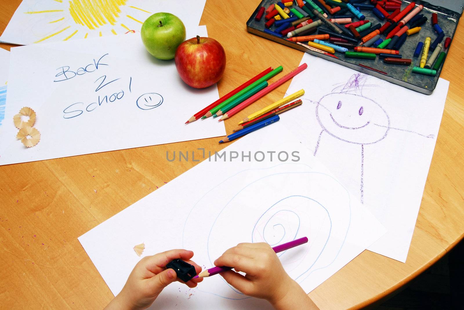 Little hands sharpening a pencil between school supplies and apples.