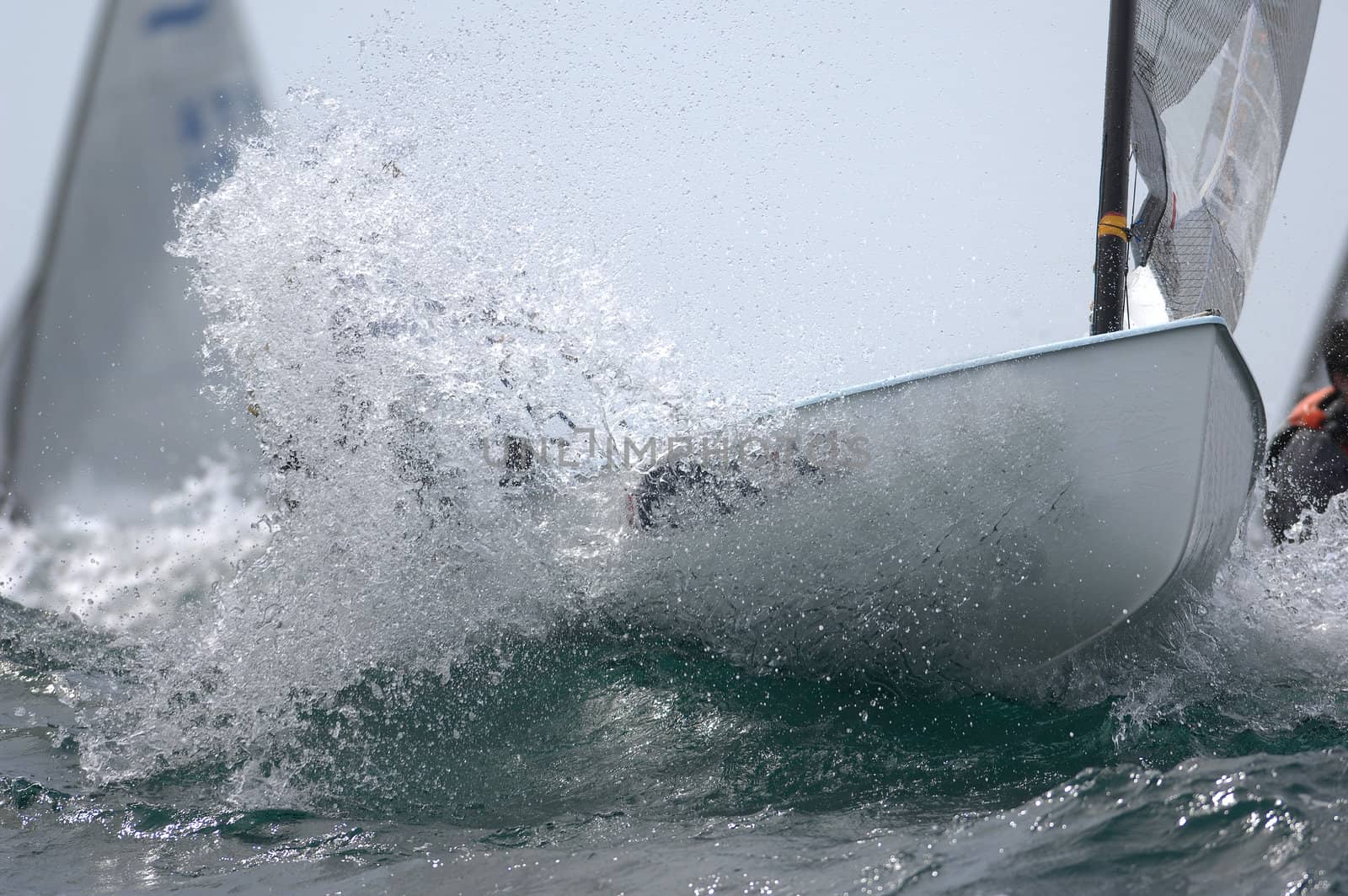 A small sail boat blasting through a wave during a race. 