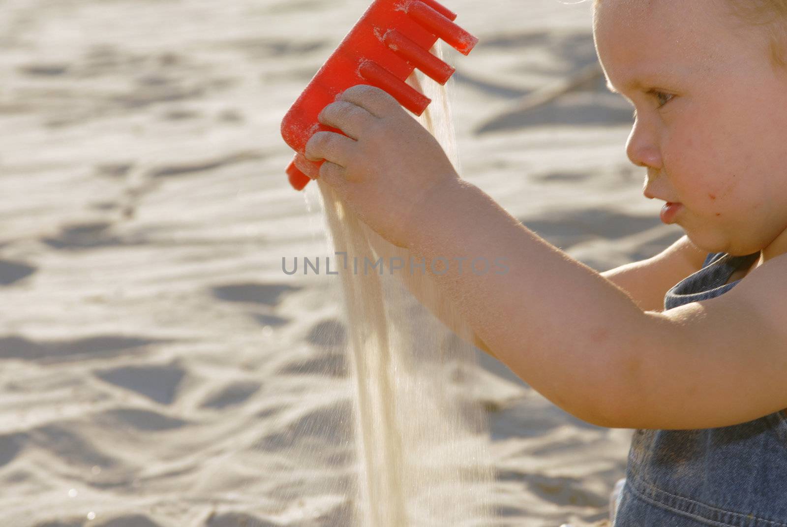 Baby girl playing on the beach with a red toy and sand. Close view