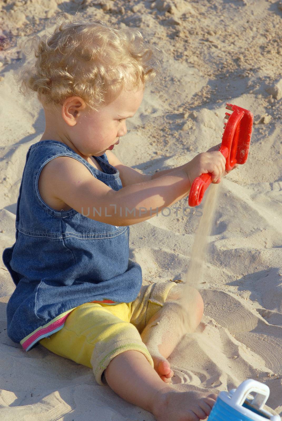 Baby girl playing on the beach with a red toy and sand. 