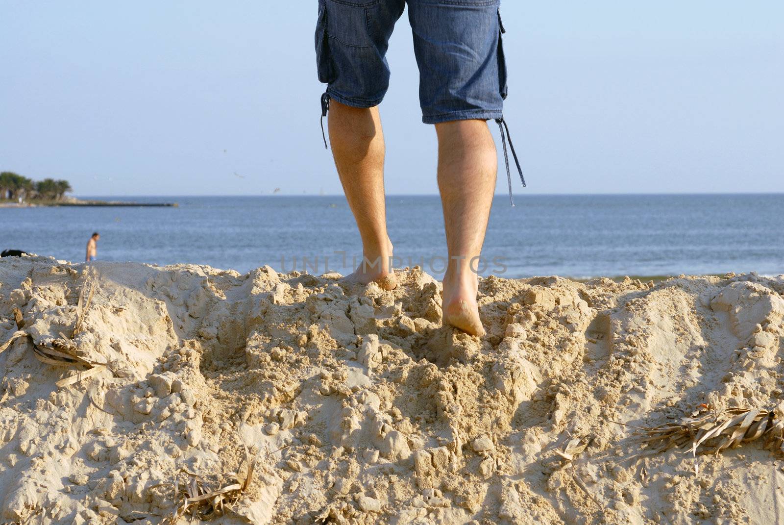 Man's legs on top of a sand dune, walking toward the sea