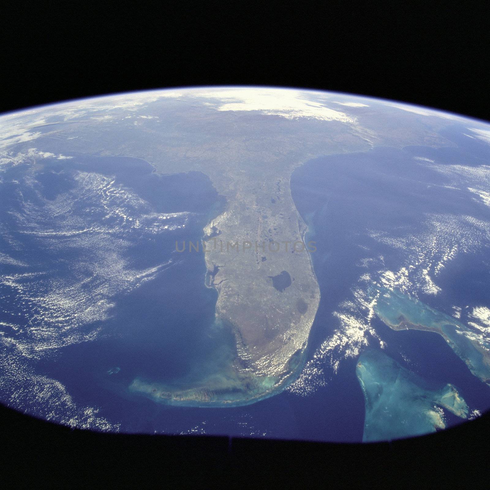 Taken during the STS-95 mission from a point over Cuba, this photo shows an oblique, foreshortened view of the Florida Peninsula, with the light blue, shallow seafloor of both the Florida Keys (curving across the bottom of the view) and the Bahama banks (right). "Popcorn" cumulus cloud covers Miami and the Southern Everglades, although the built-up area from Ft. Lauderdale to West Palm Beach can be discerned. Lake Okeechobee is the prominent waterbody in Florida. Cape Canaveral is shown well, half way up the peninsula. Photo taken: 10/31/1998. ** Credit: NASA / yaymicro.com **