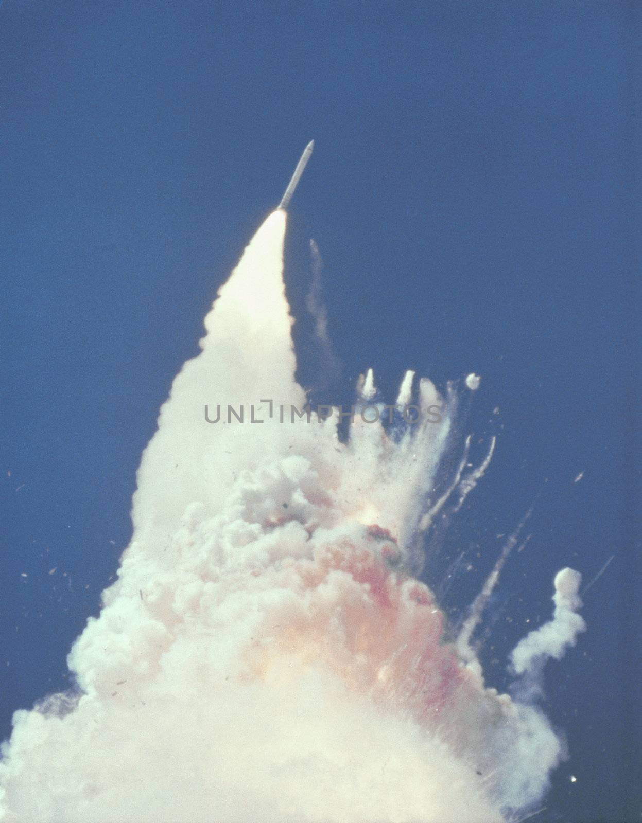 At about 76 seconds, fragments of the Orbiter can be seen tumbling against a background of fire, smoke and vaporized propellants from the External Tank. The left Solid Rocket Booster (SRB) flys rampant, still thrusting. The reddish-brown cloud envelops the disintergrating Orbiter. The color is indicative of the nitrogen tetroxide oxidizer propellant in the Orbiter Reaction Control System. On January 28, 1986 frigid overnight temperatures caused normally pliable rubber O-ring seals and putty that are designed to seal and establish joint integrity between the Solid Rocket Booster (SRB) joint segments, to become hard and non- flexible. At the instant of SRB ignition, tremendous stresses and pressures occur within the SRB casing and especially at the joint attachment points. Photo taken: 01/28/1986. ** Credit: NASA / yaymicro.com **