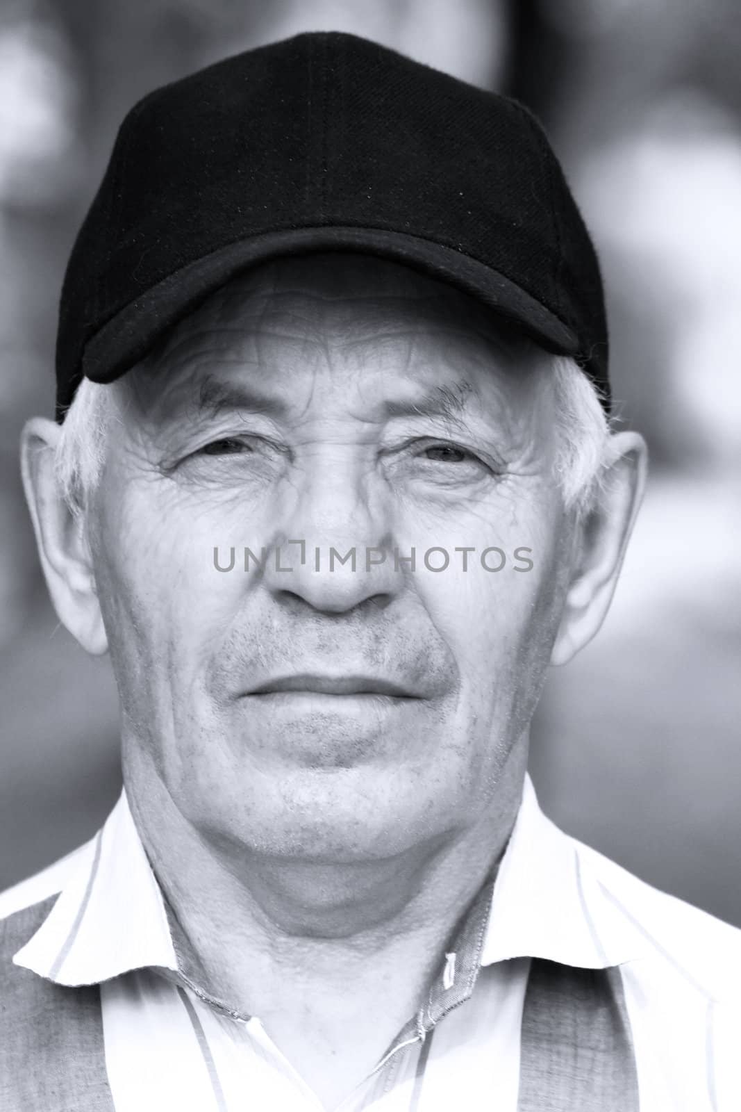 Portrait of the elderly man in a cap and a striped shirt against the nature