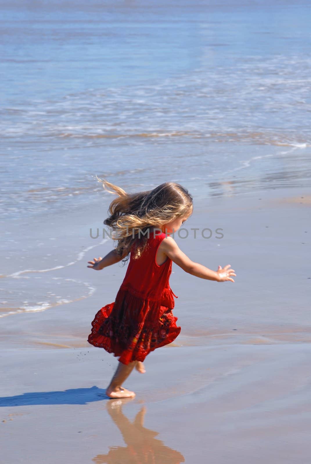 Happy girl on the beach, in a red beautiful dress, playing at the seashore