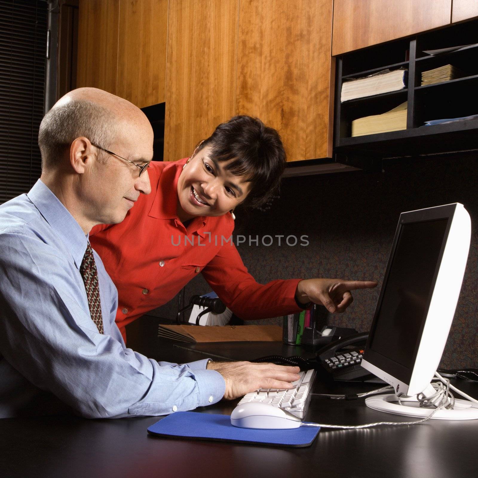 Businessman and businesswoman in office smiling looking and pointing at computer monitor.