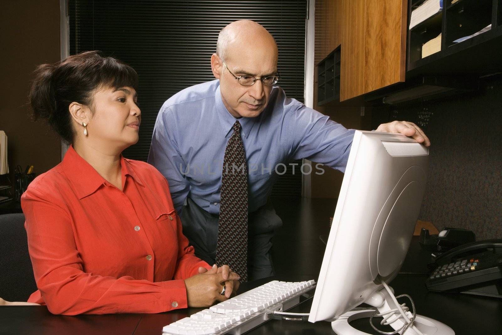 Businessman and businesswoman in office looking at computer monitor.