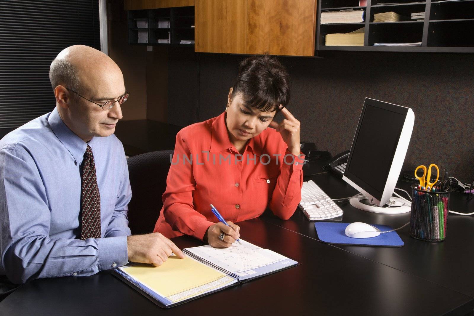 Businessman and businesswoman in office going over appointment calendar.