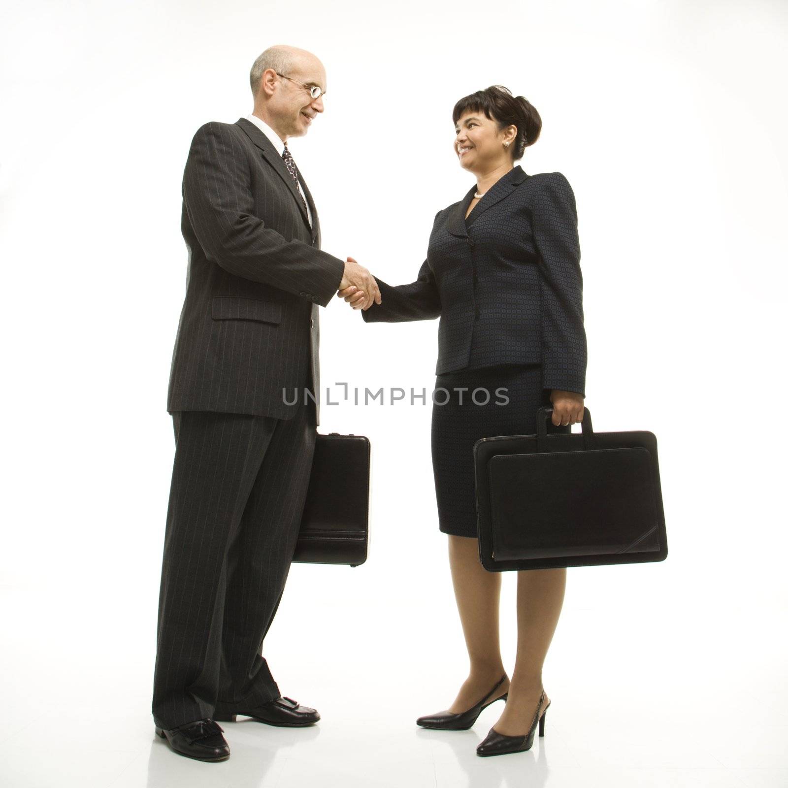 Caucasian middle-aged businessman and Filipino businesswoman standing looking at eachother shaking hands against white background.
