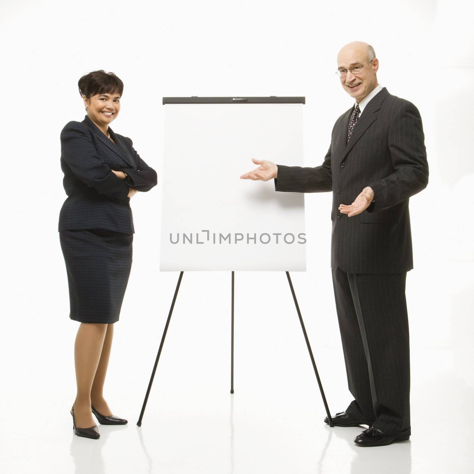 Smiling Caucasian middle-aged businessman and Filipino businesswoman standing making presentation against white background.