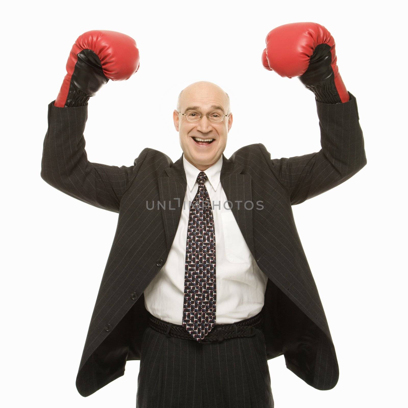 Smiling Caucasian middle-aged businessman standing with arms raised wearing boxing gloves.