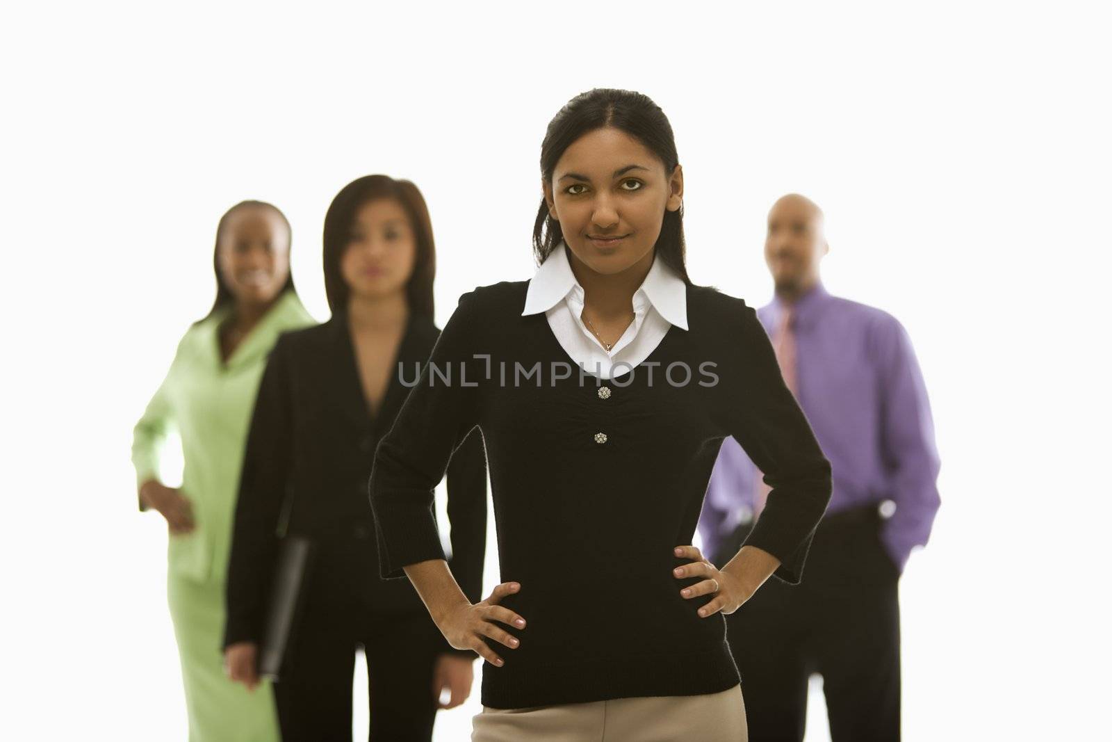 Portrait of Indian businesswoman smiling with hands on hips with others in background.