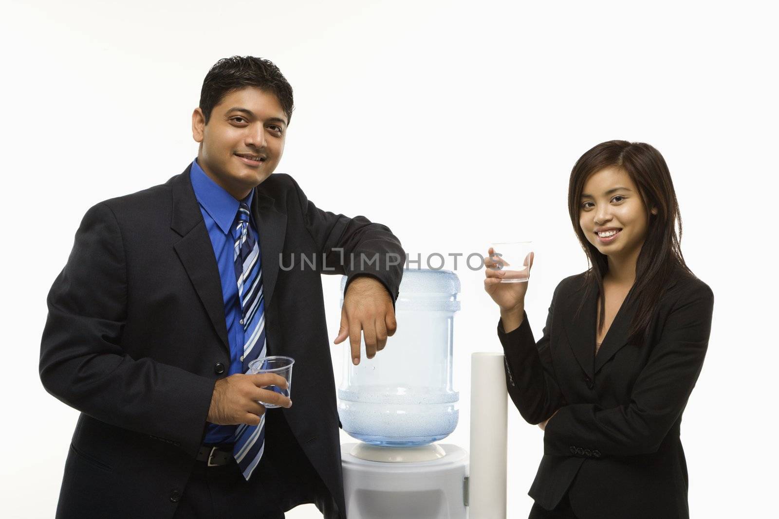 Vietnamese businesswoman and Indian standing at water cooler looking at viewer.