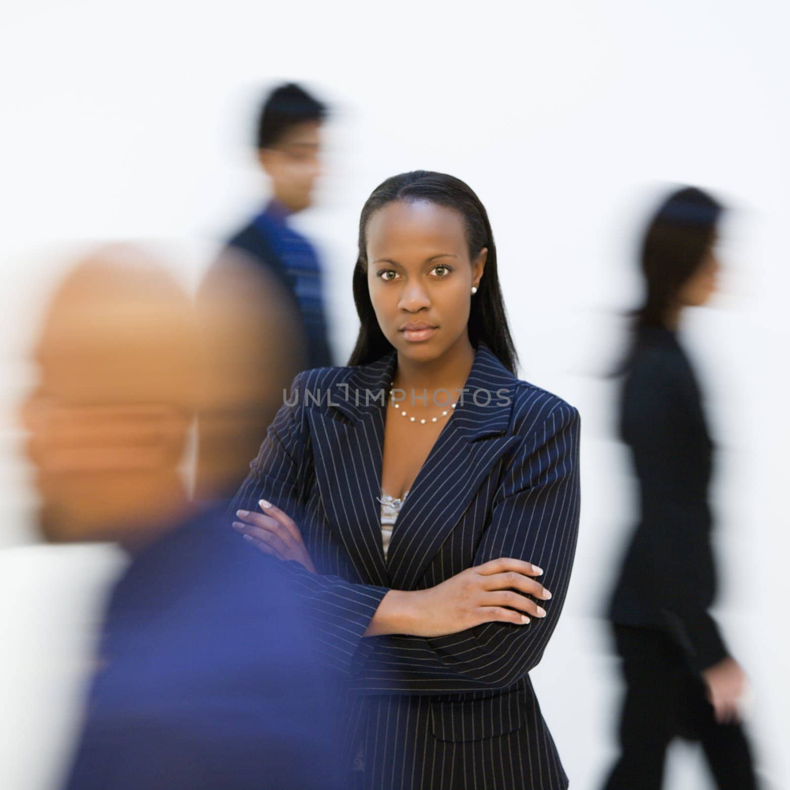 African-American businesswoman standing with arms crossed while others walk by.