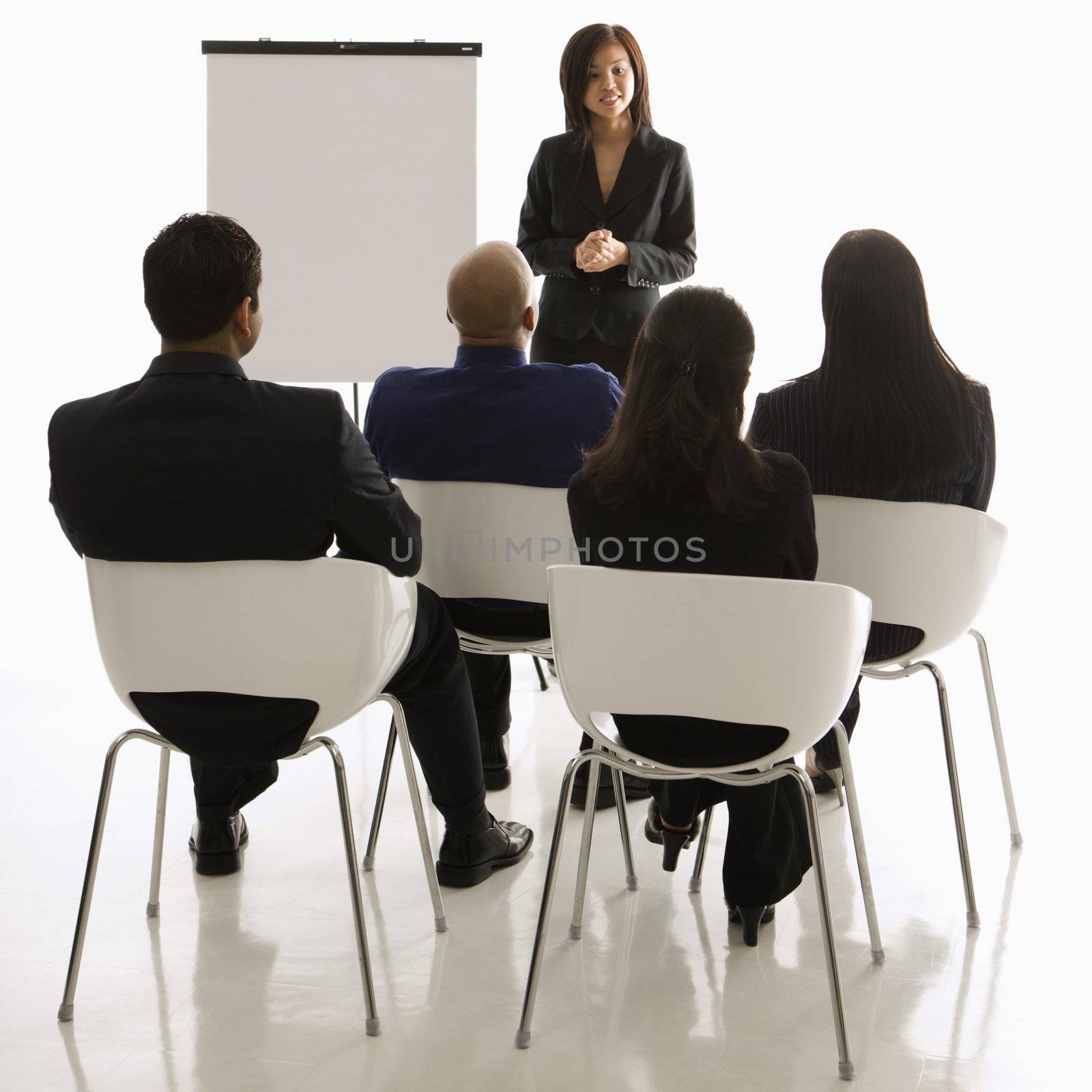 Vietnamese mid-adult woman standing in front of business group leading presentation.