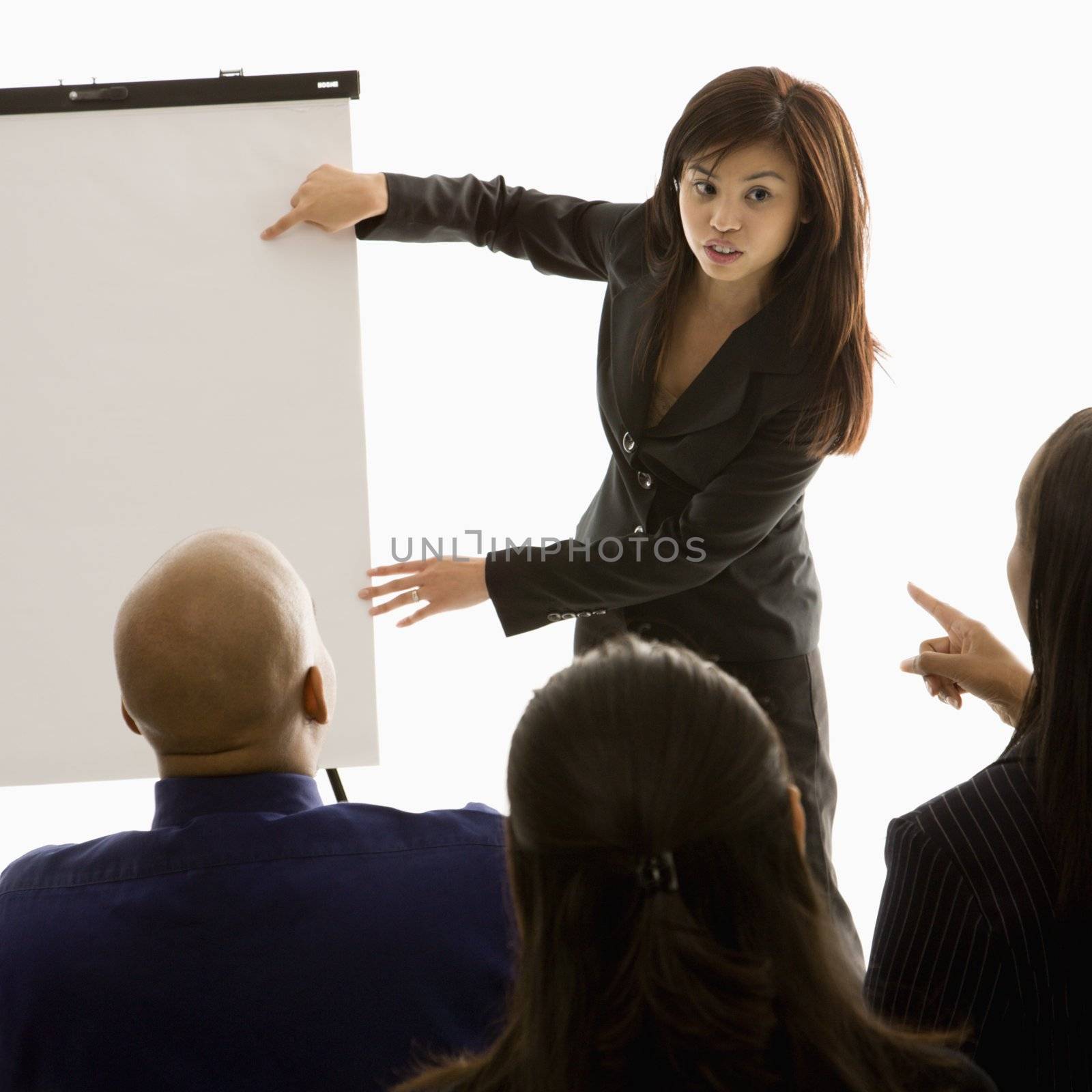 Vietnamese mid-adult woman standing in front of business group pointing to presentation.