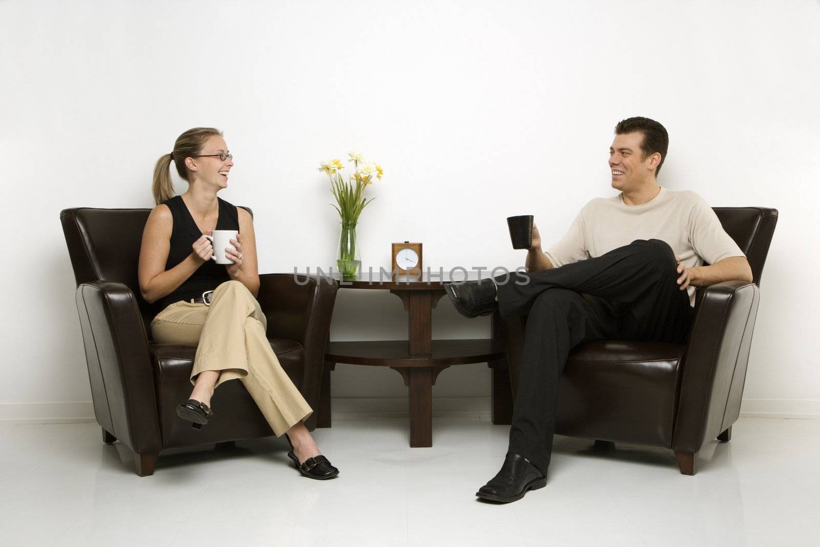 Caucasian mid-adult man and woman sitting in armchairs drinking coffee.