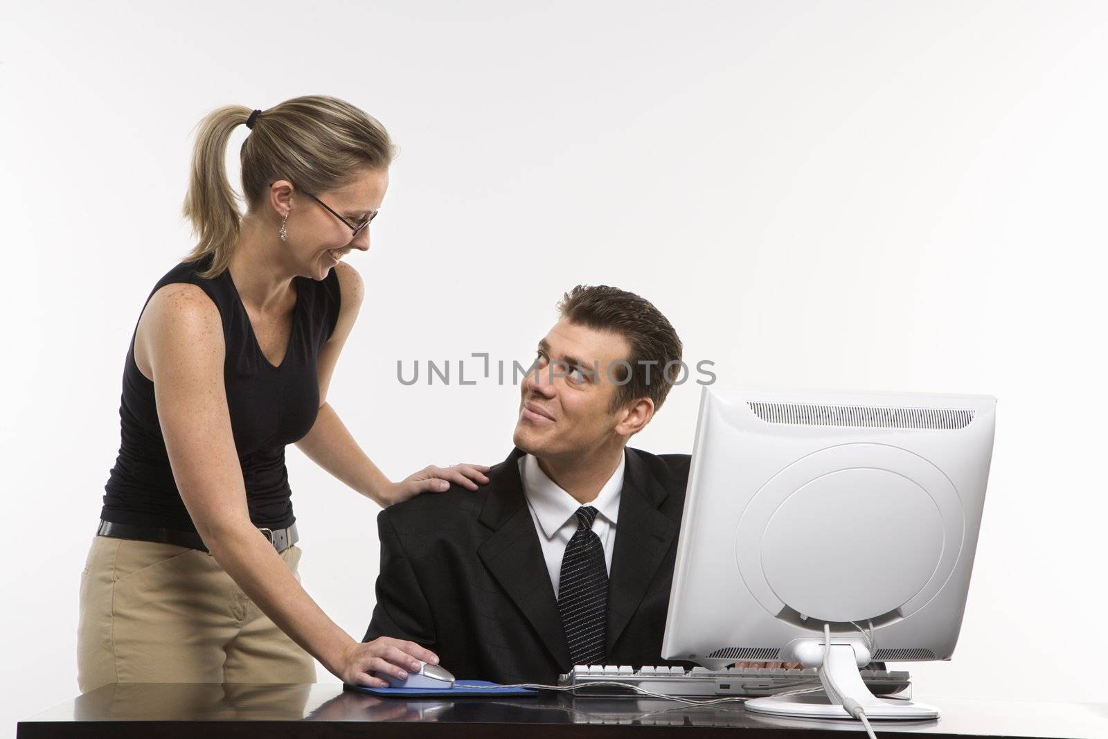 Caucasian mid-adult woman touching mid-adult man's shoulder and using mouse at computer.