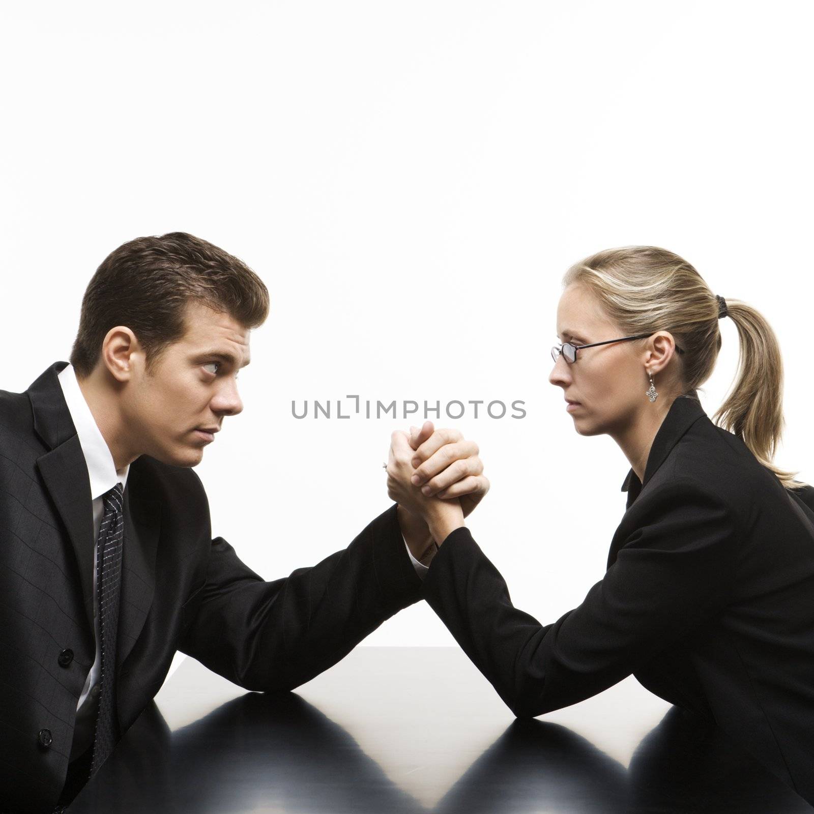 Side view of Caucasian mid-adult businessman and businesswoman arm wrestling on table.