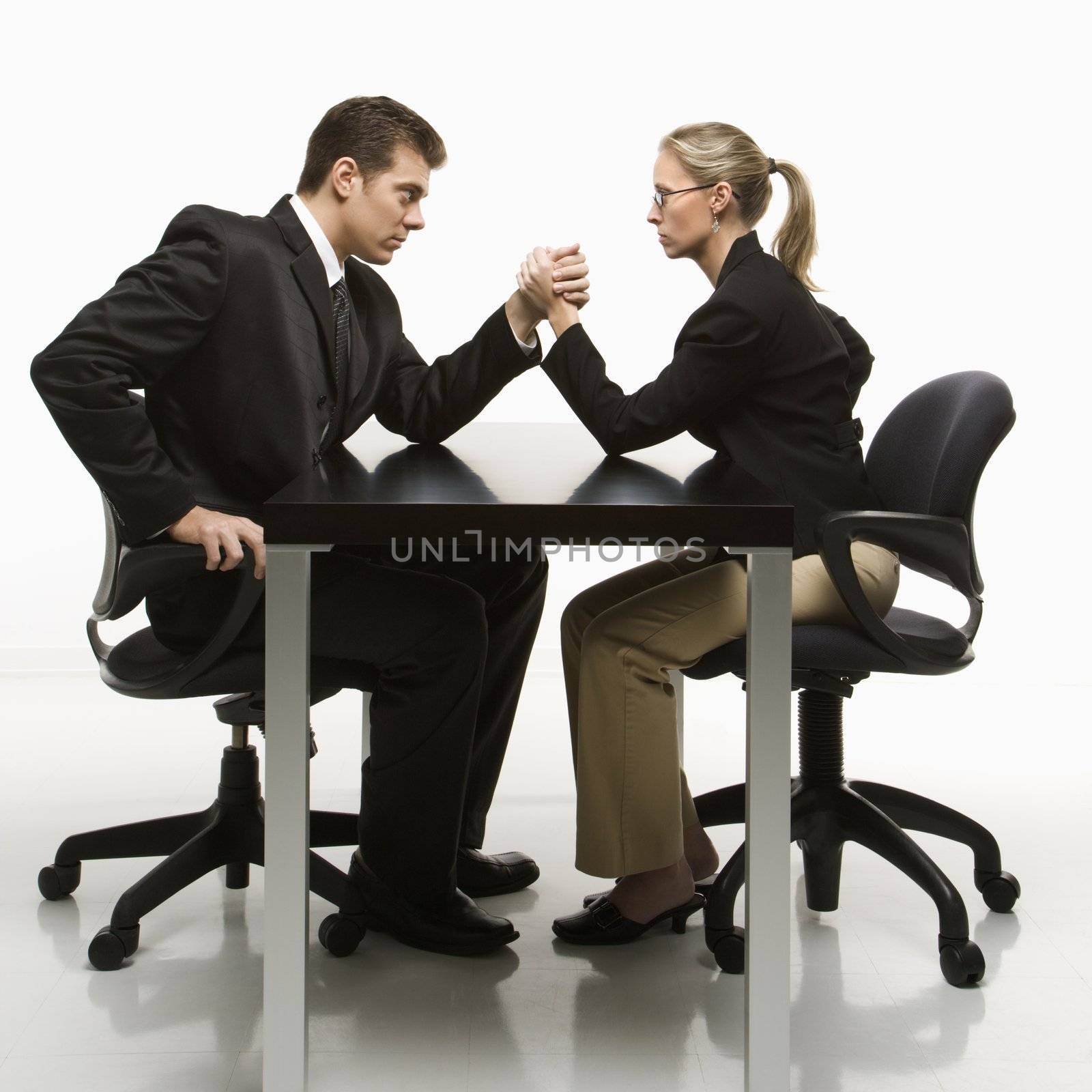 Side view of Caucasian mid-adult businessman and businesswoman arm wrestling on table.