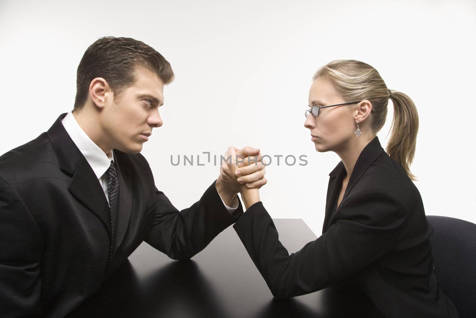 Side view of Caucasian mid-adult businessman and businesswoman arm wrestling on table.