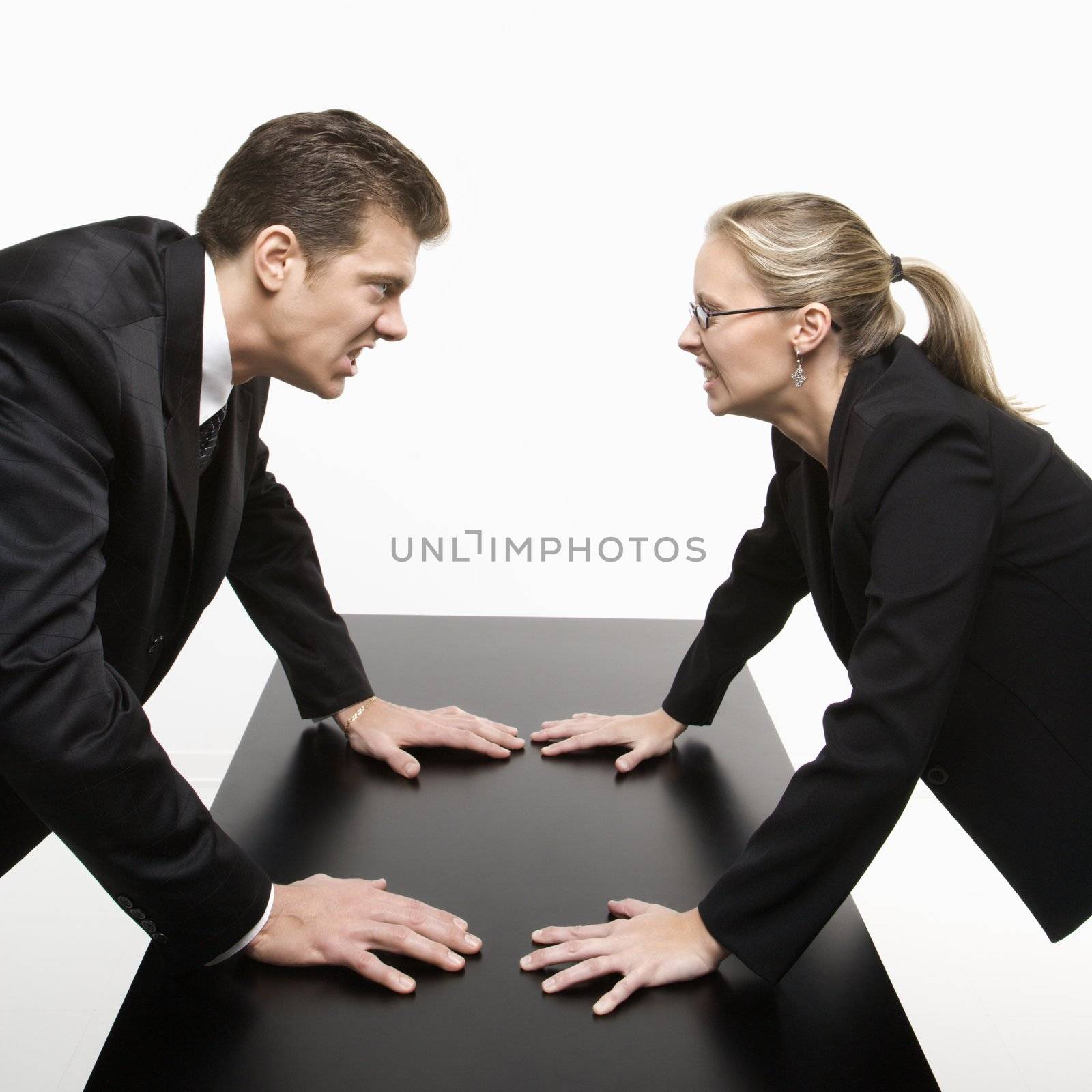 Caucasian mid-adult businessman and woman staring at each other with hostile expressions.