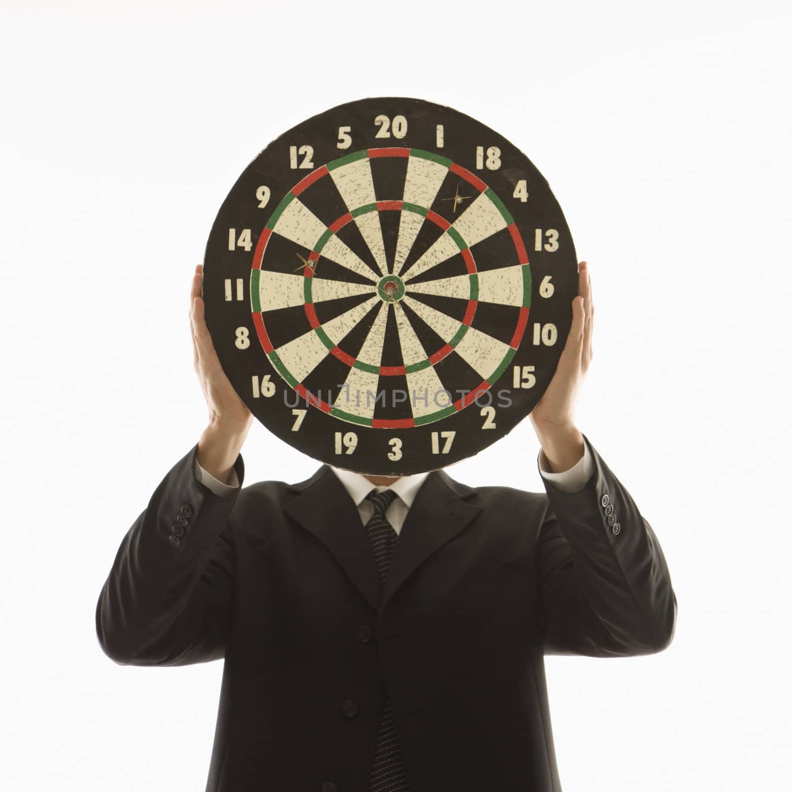 Caucasian man wearing suit and holding dartboard in front of face.