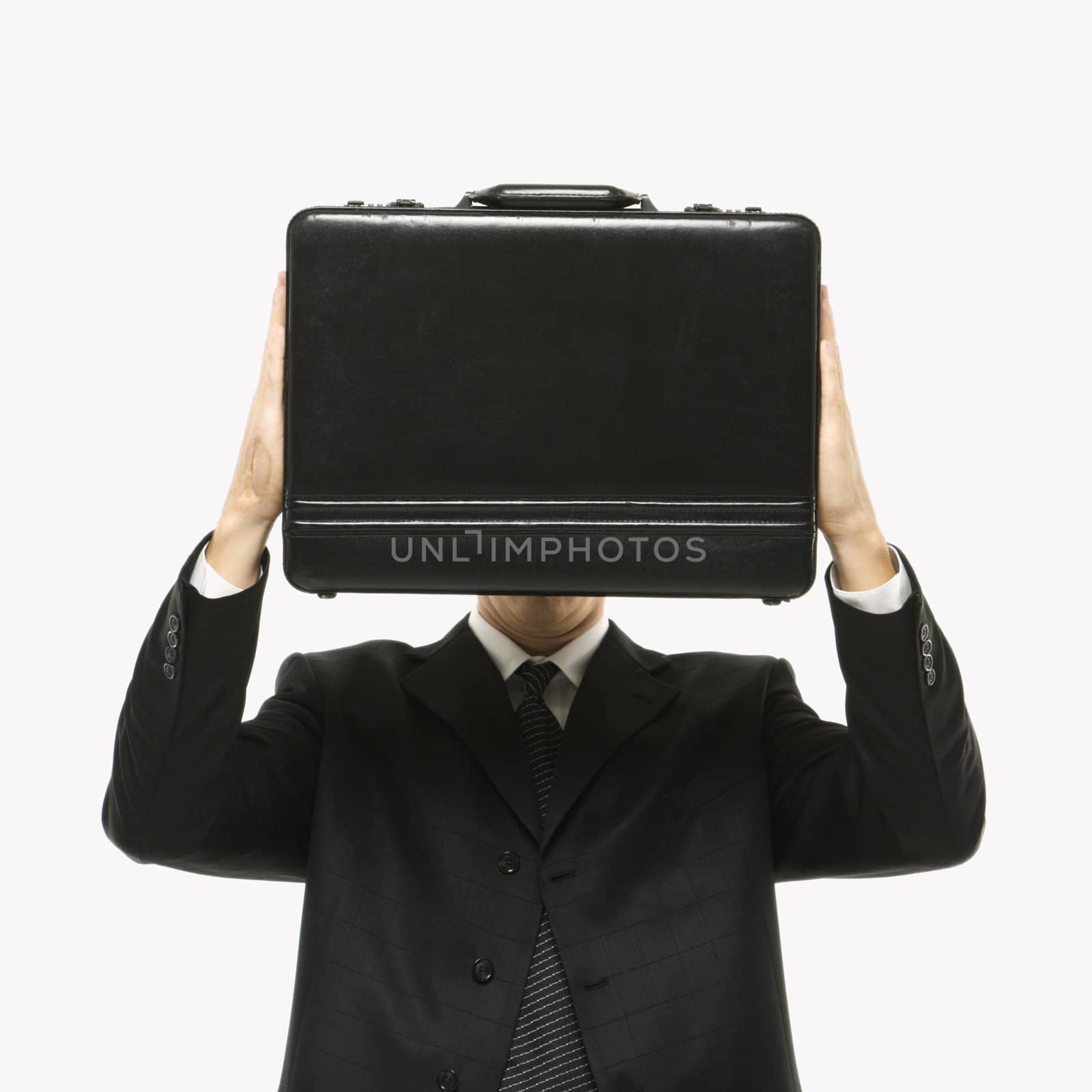 Caucasian man wearing suit and holding briefcase in front of face.