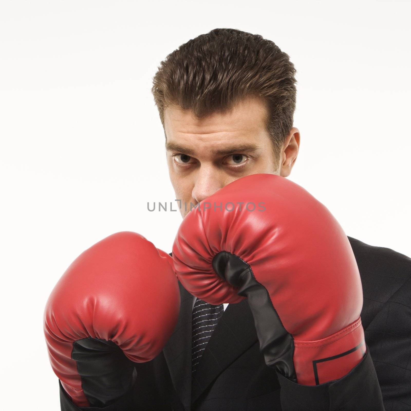 Caucasian mid-adult man wearing suit and holding boxing gloves close to his face.