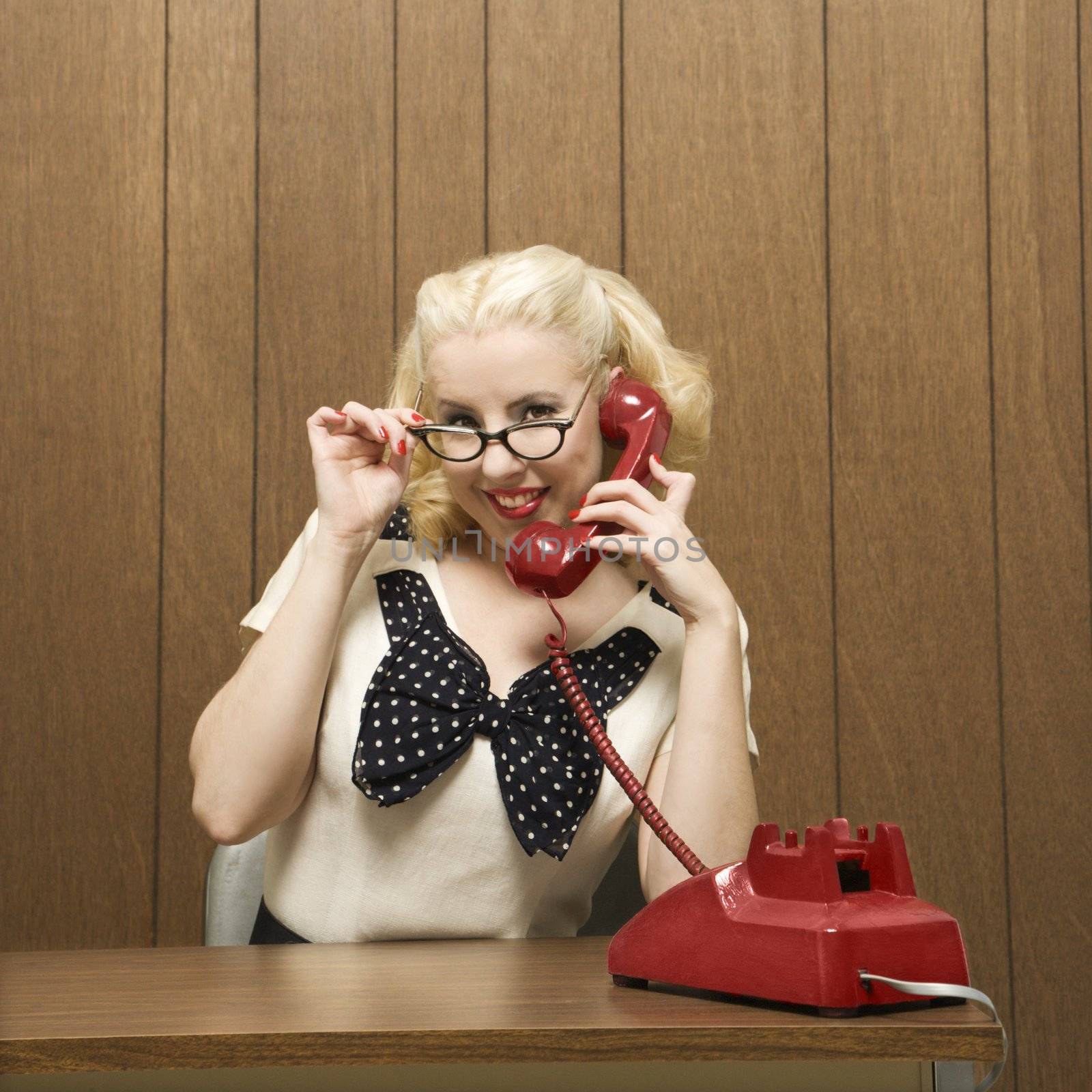 MId-adult Caucasian female dressed in retro outfit holding a red phone.