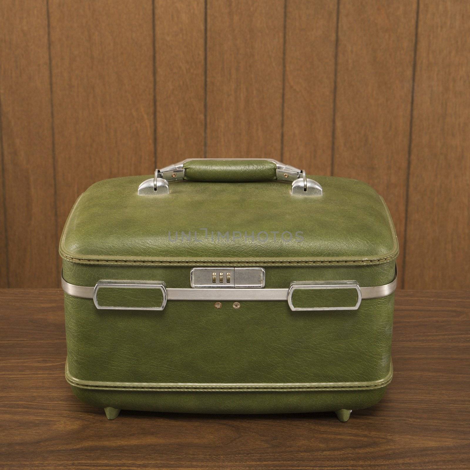 Still life shot of a vintage green luggage piece sitting on a wooden desk.