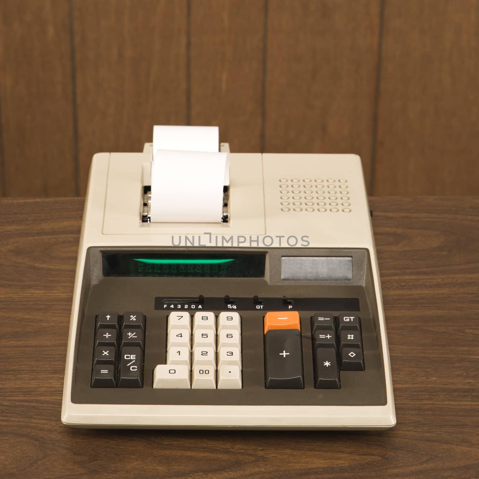 Still life shot of a vintage adding machine sitting on a wooden desk.