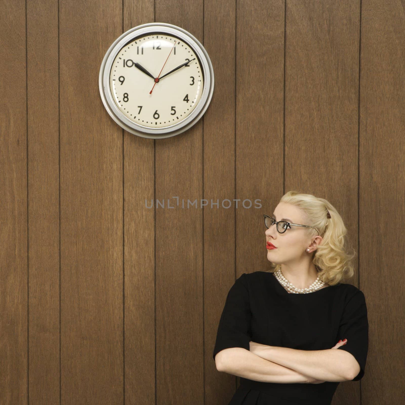 Mid-adult Caucasian female in vintage outfit looking up at clock.