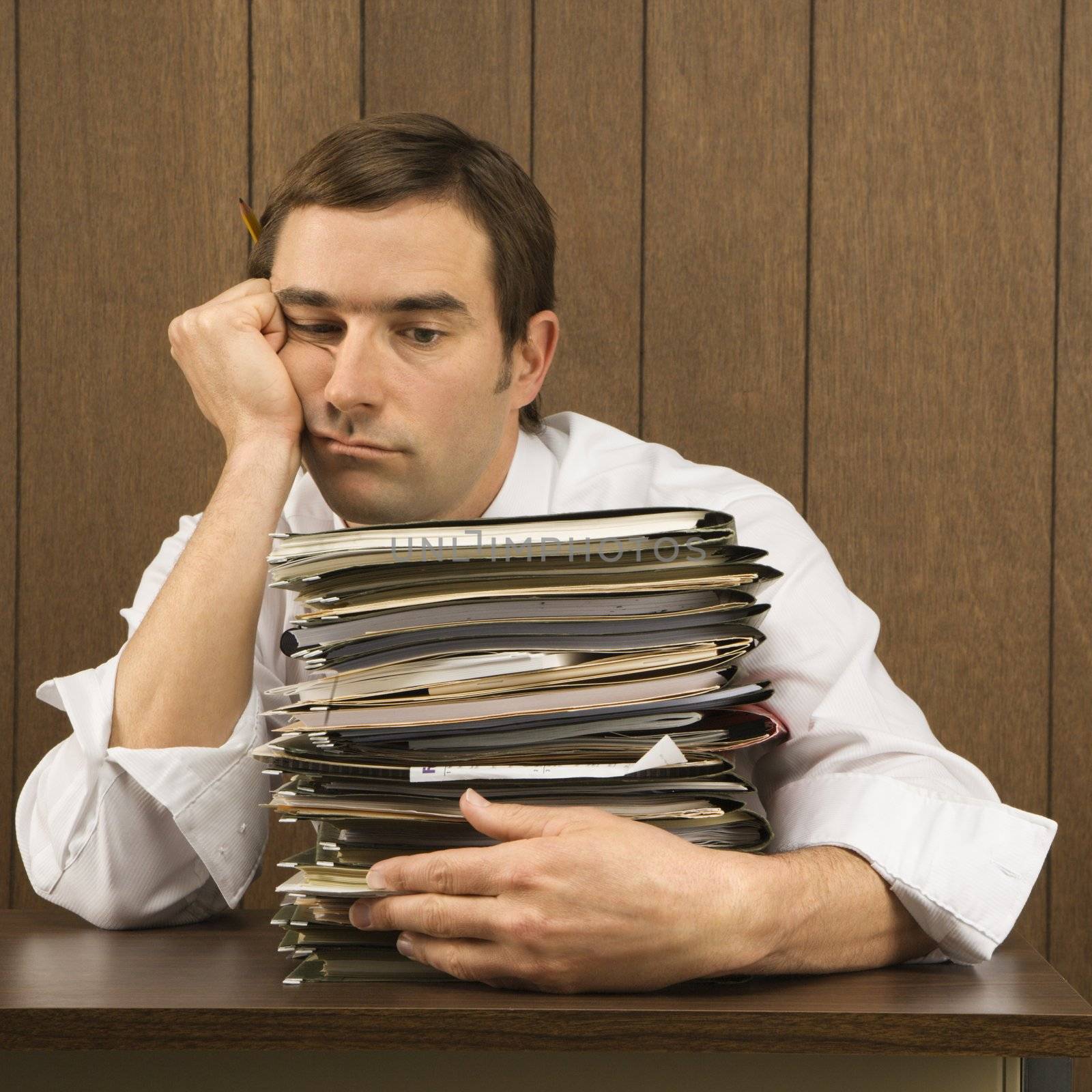 Mid-adult Caucasian male with overwhelmed face holding lots of paperwork