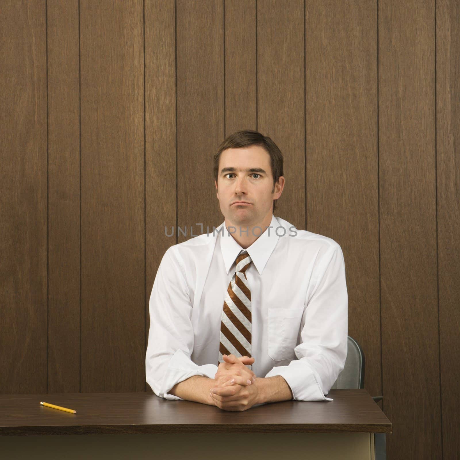 Mid-adult Caucasian male sitting at desk with pencil beside him.