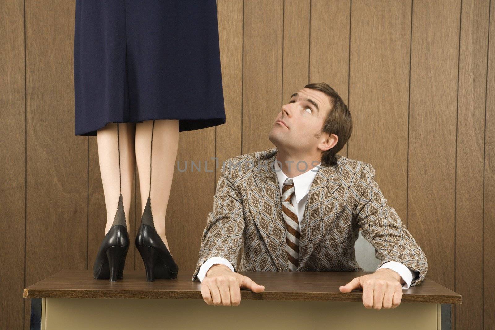 Mid-adult Caucasian male holding desk looking up to Caucasian female standing on desk.