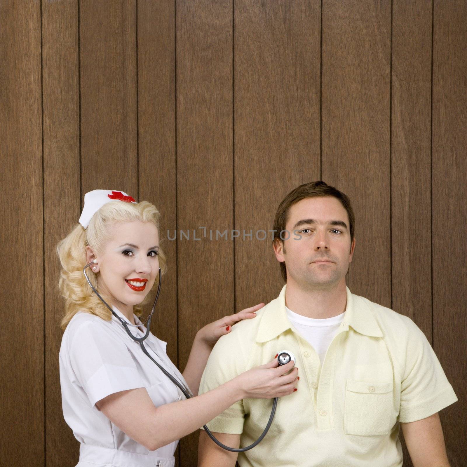 Caucasian mid-adult female nurse checking male's heartbeat by wood paneling.