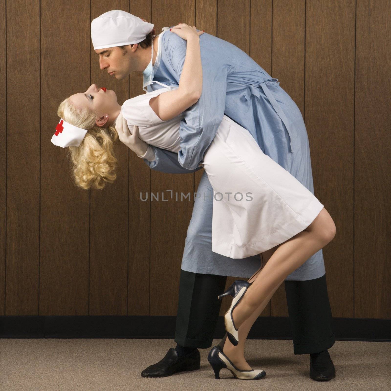 Mid-adult Caucasian male surgeon bending female nurse over backwards for passionate embrace.