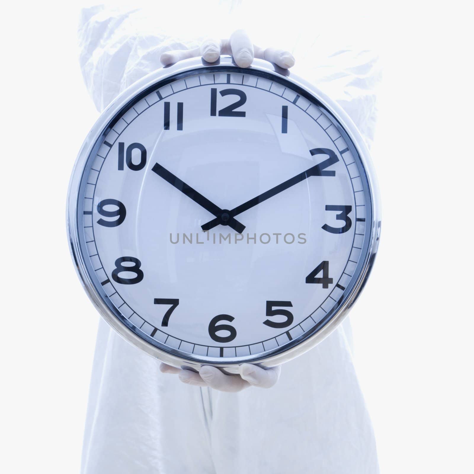 Man in biohazard suit holding out clock standing against white background.