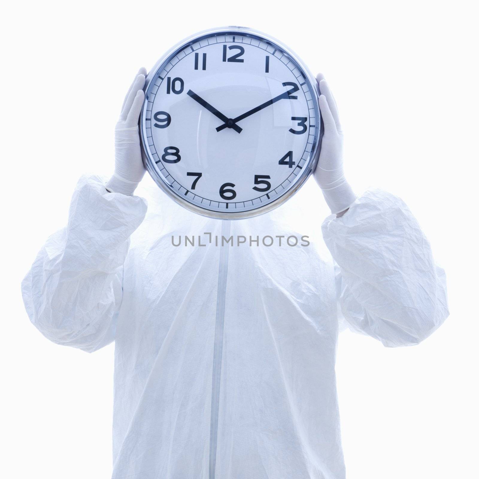 Man in biohazard suit holding clock in front of face standing against white background.