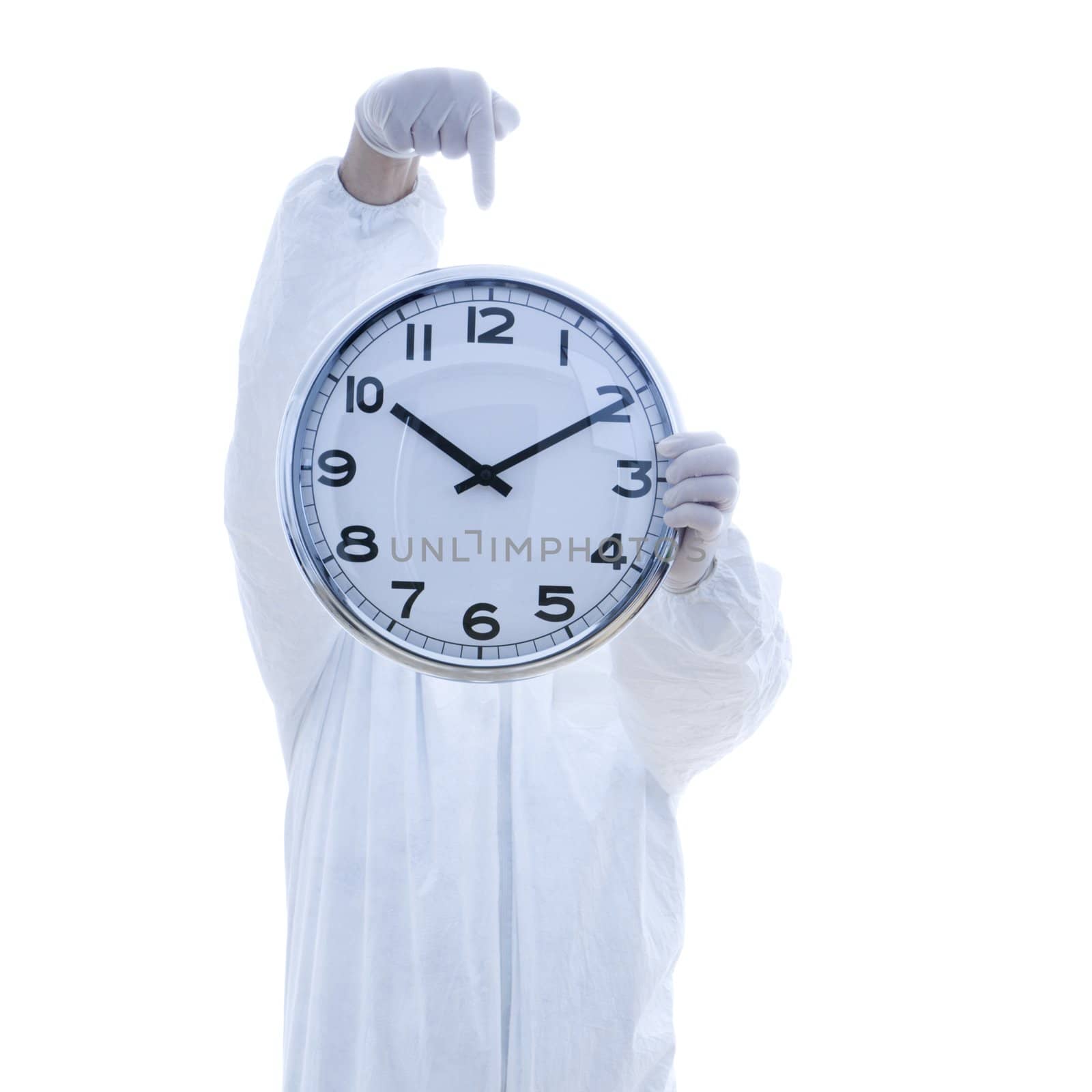 Man in biohazard suit holding clock in front of face pointing to clock with finger standing against white background.