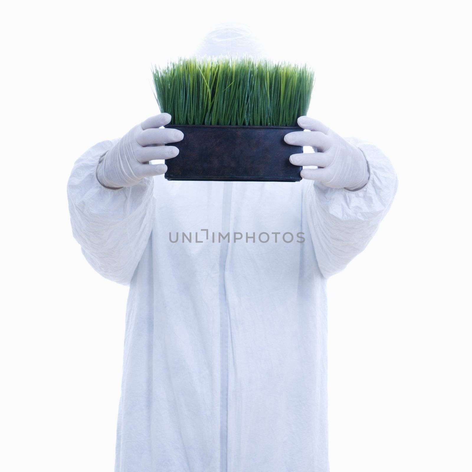 Man in biohazard suit holding pot of grass in front of face standing against white background.