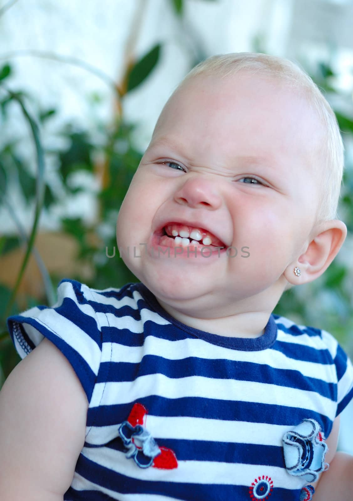 Little girl with blond hair smiling and grimacing on green plant background.